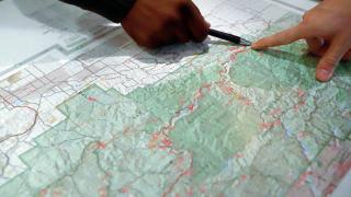 Image shows two people's hands pointing at a location on a topographic map of a national forest.
