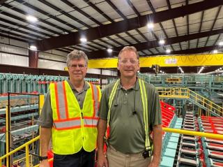 Image shows two men in high-visibility gear in a manufacturing facility.