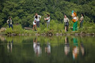 Image shows Woodsy Owl and several women picking up litter along a lakeshore.