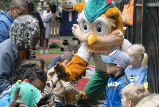 Image shows Woodsy Owl giving children a high five while adults look on.