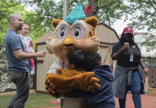 Image shows Woodsy Owl giving children a hug while adults look on.