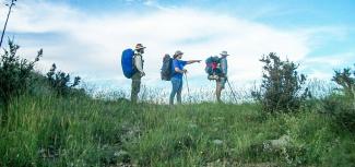 Three backpackers pause on the trail overlooking a valley.