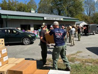 Line of USFS Firefighters pass boxes of supplies from a trailer to pallet