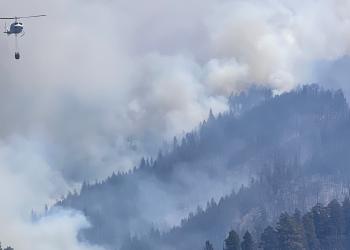 Helicopter dropping water on a fire with smoke in the mountains