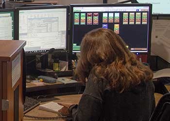 Dispatcher writing on paper in front of multiple computer screens.