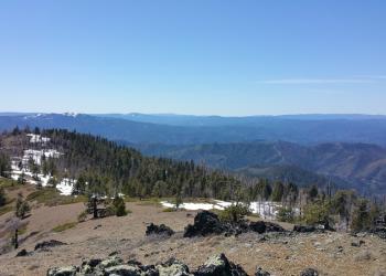 Wooded ridges are seen from a mountain top under blue skies.