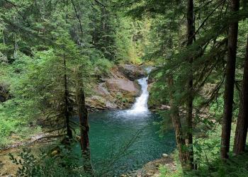 Waterfall, falling into a blue-green pool surrounded by lush green forest.