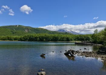 This image is showing the view from the start of the LAkes trail near Coldwater lake. The lake can be seen in the foreground with the Birth of a Lake boardwalk trail visual as well. Mount St Helens can be partially seen with a cloud covering the top in the background.