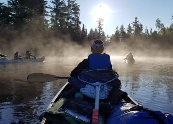 people canoeing on a lake through fog