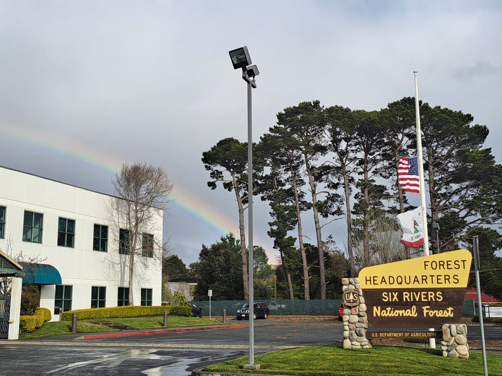 A picture of the sign and office of Six Rivers National Forest's Headquarters, a rainbow can be seen behind the office