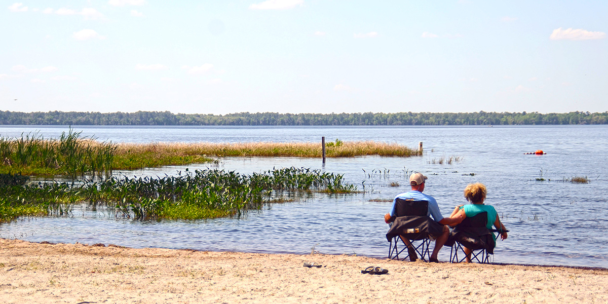 A lake beach with two people sitting in chairs.