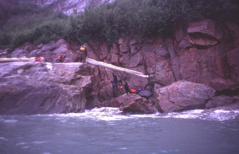 Kayakers clad in rain gear lift their boats up onto a rock shelf on a steep ocean shore.