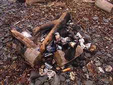 A campfire brims with beer bottles, foil, melted plastic and paper trash.