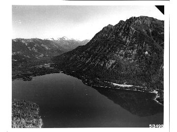 Aerial view of the upper end of Lake Wenatchee. Dirty - faced Mountain is at right. Lake Wenatchee Ranger Station is at base of the mountain. White River drainiage is at left. Snow covered Glacier Peak can be seen in the distance.