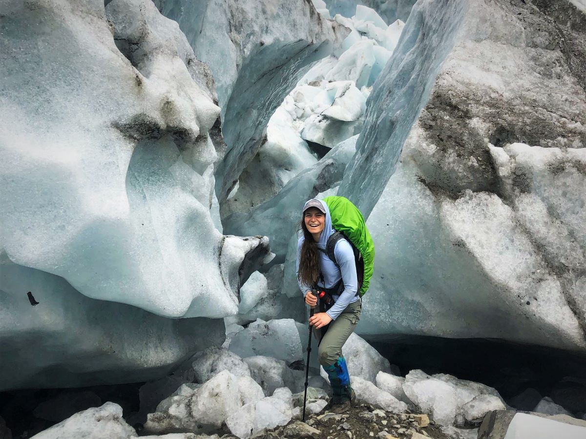 Artist Theresa Ptak stands in front of the toe of a glacier.