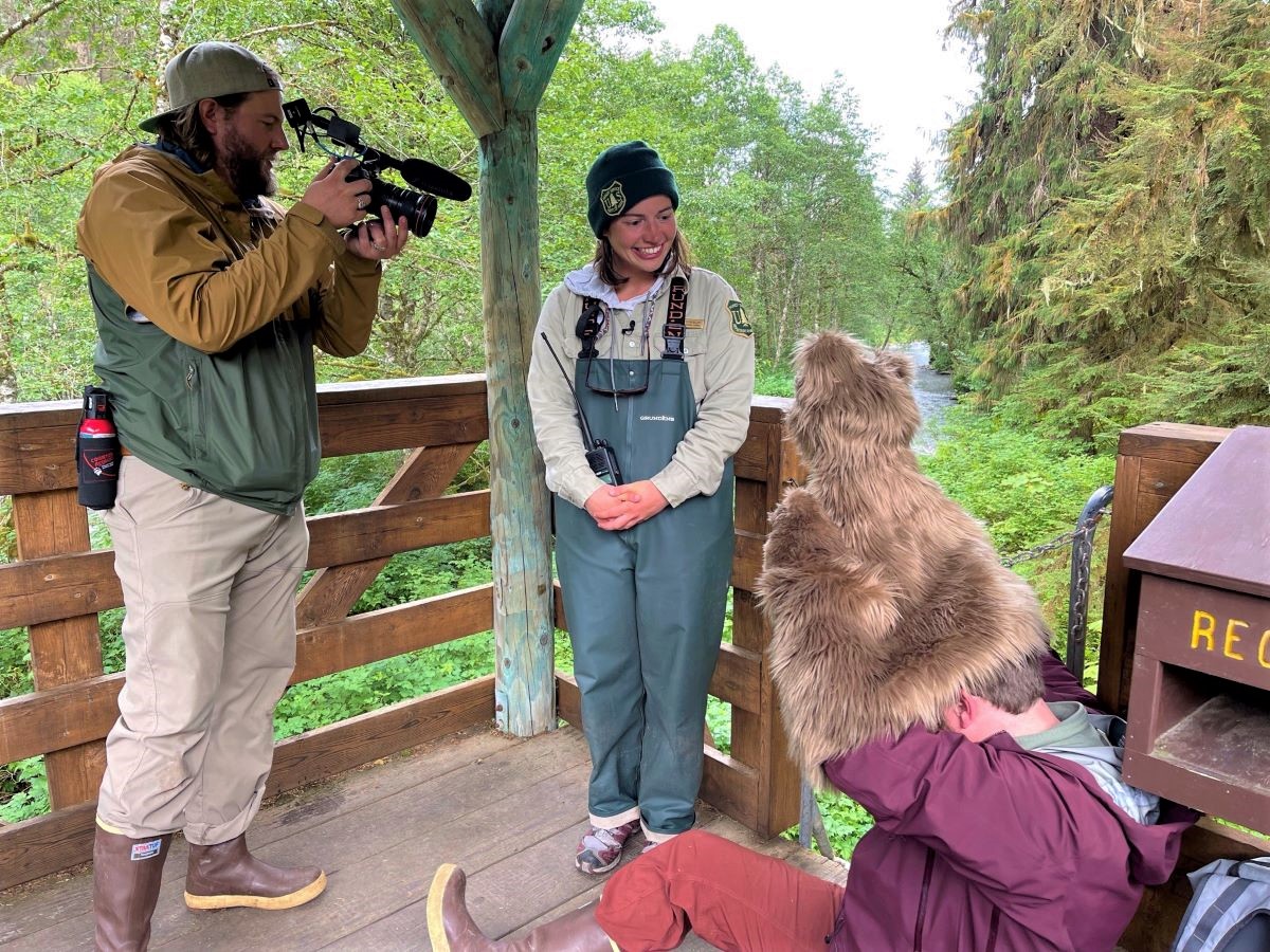 A videographer filming a ranger who is talking to a bear puppet.