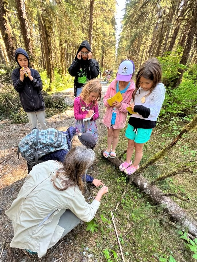 A woman crouches down during a nature walk with kids.