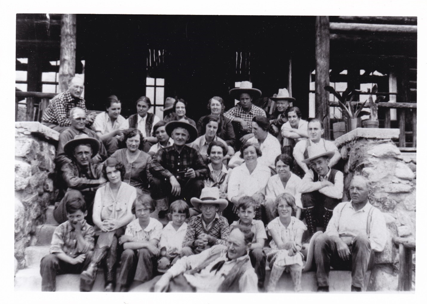 A black and white photo of a large group of people sitting on the steps of a lodge.