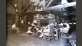 About ten people sitting inside a wooden lodge with a fireplace.