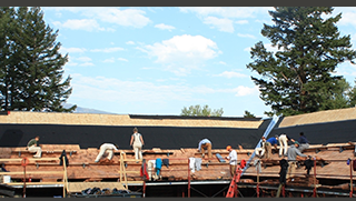 A photo of about 16 people working on a wide roof of a lodge.