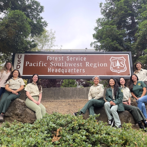 Several people sitting and posing around the Regional Office sign for the USDA Forest Service Pacific Southwest Region.