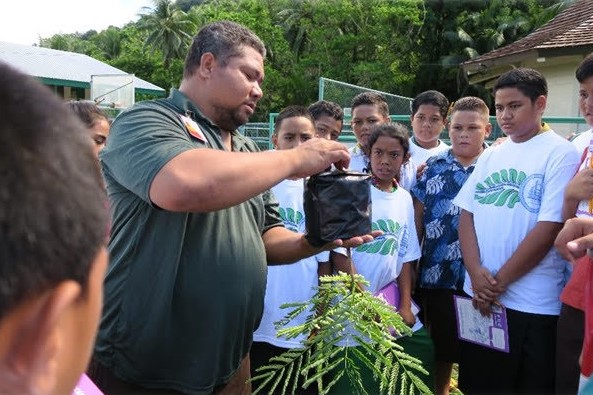Man in front of group of students with seedlings and tree.