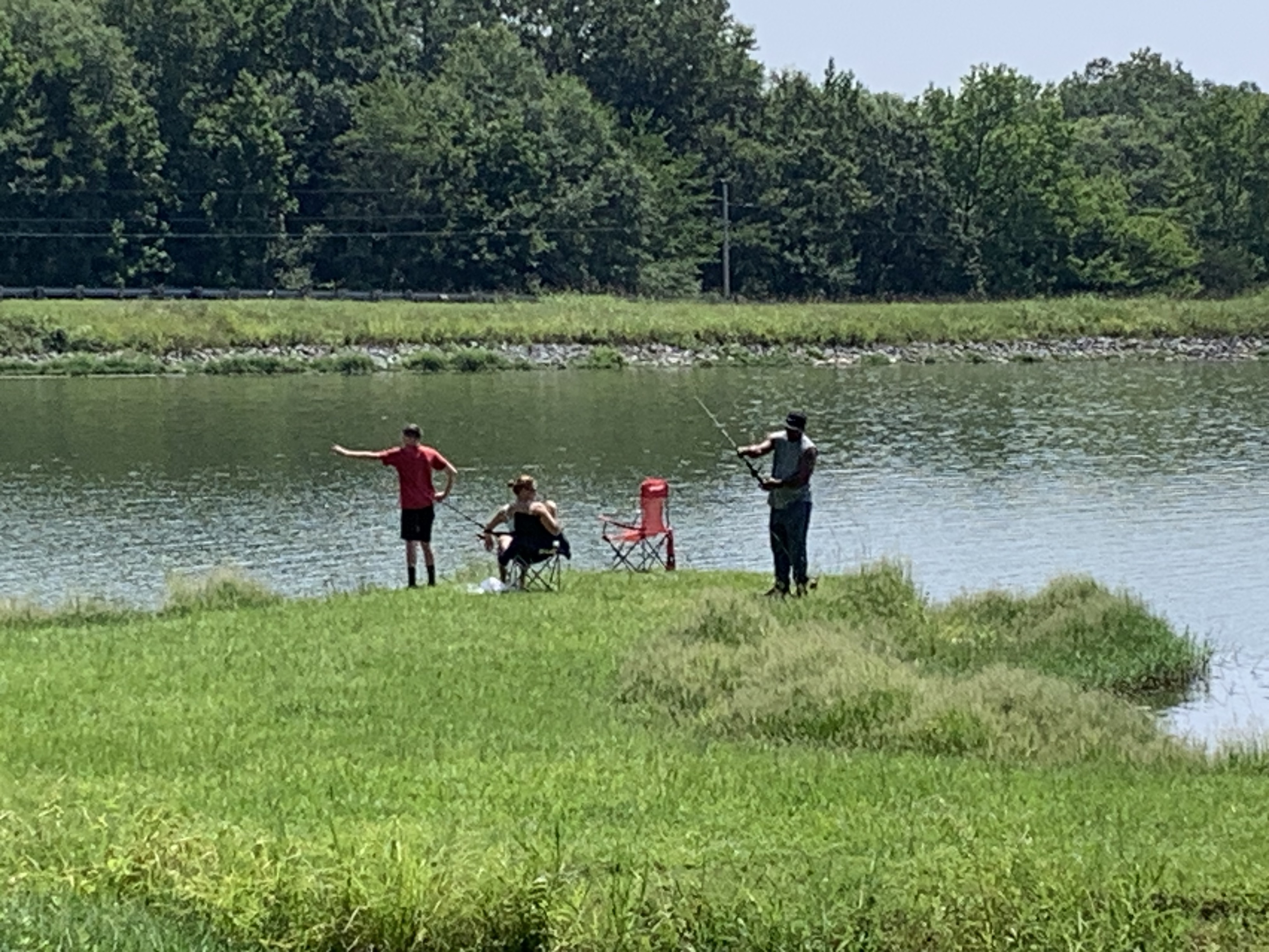Three people along the bank of a lake holding fishing poles.