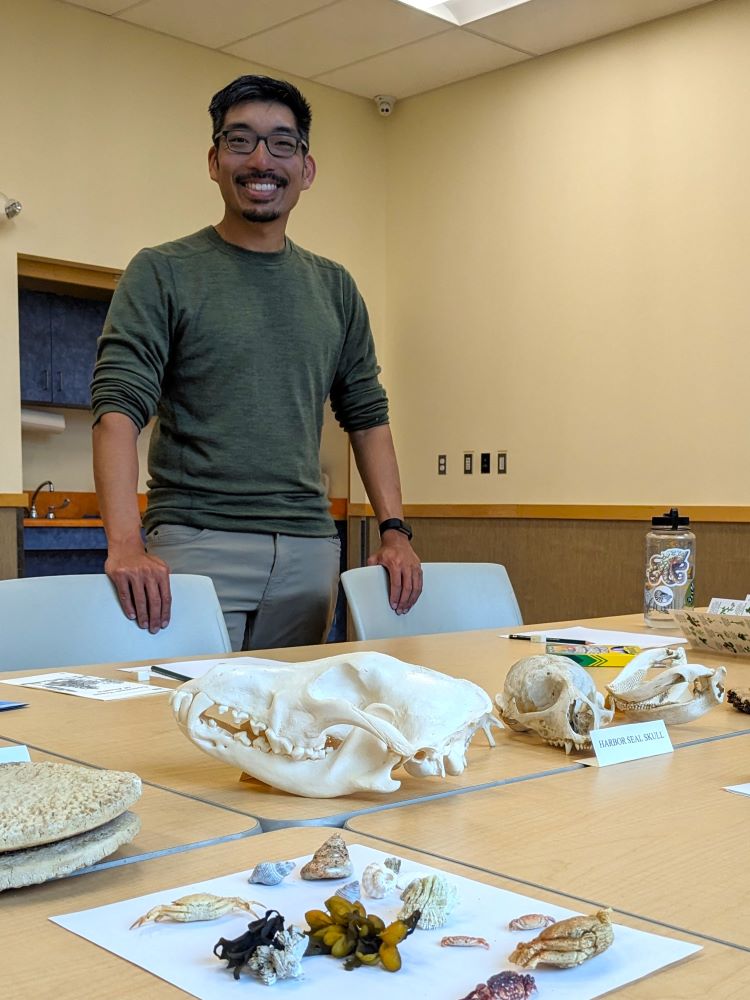 Trenton Jung stands smiling over a table filled with animal skulls and other beach finds.