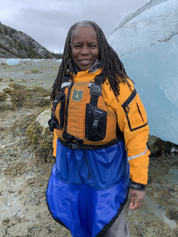 Jacqueline Scott stands near an iceberg wearing a kayak skirt.