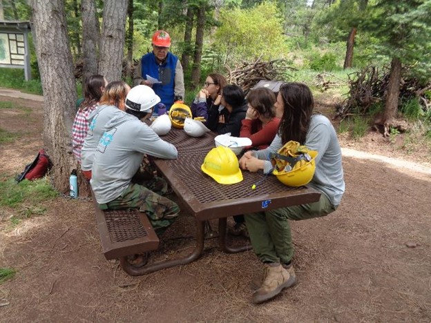 Volunteers sit at a picnic table outside listening to a field seminar