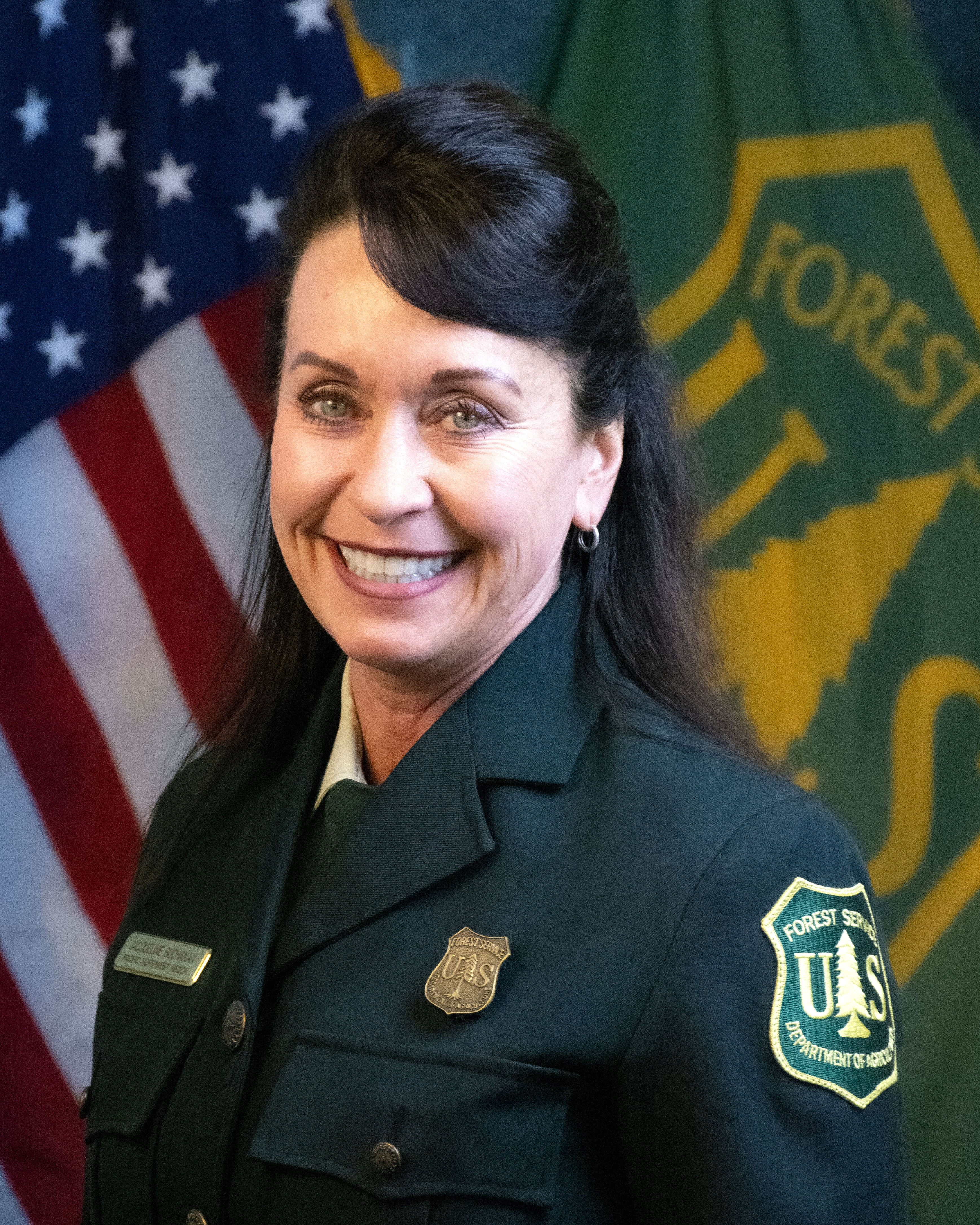 portrait showing a women in the forest service uniform with US and Forest service flags behind her.