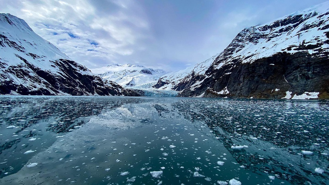 An icy bay in Prince William sound, filled with brash ice, a tidewater glacier sits in the back between snowy mountains.