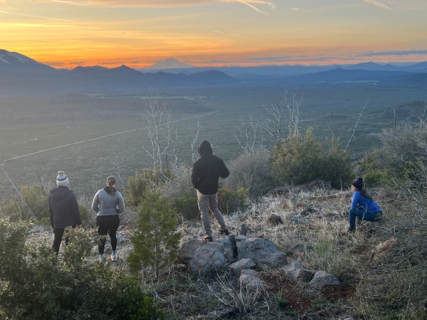 A small group of night sky viewers gather at a viewpoint as the sun goes down behind distant mountains on the Lassen National Forest.