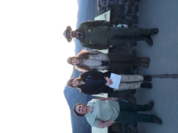 Forest Service and National Park Service employees stand at a viewpoint area with mountains in the background.