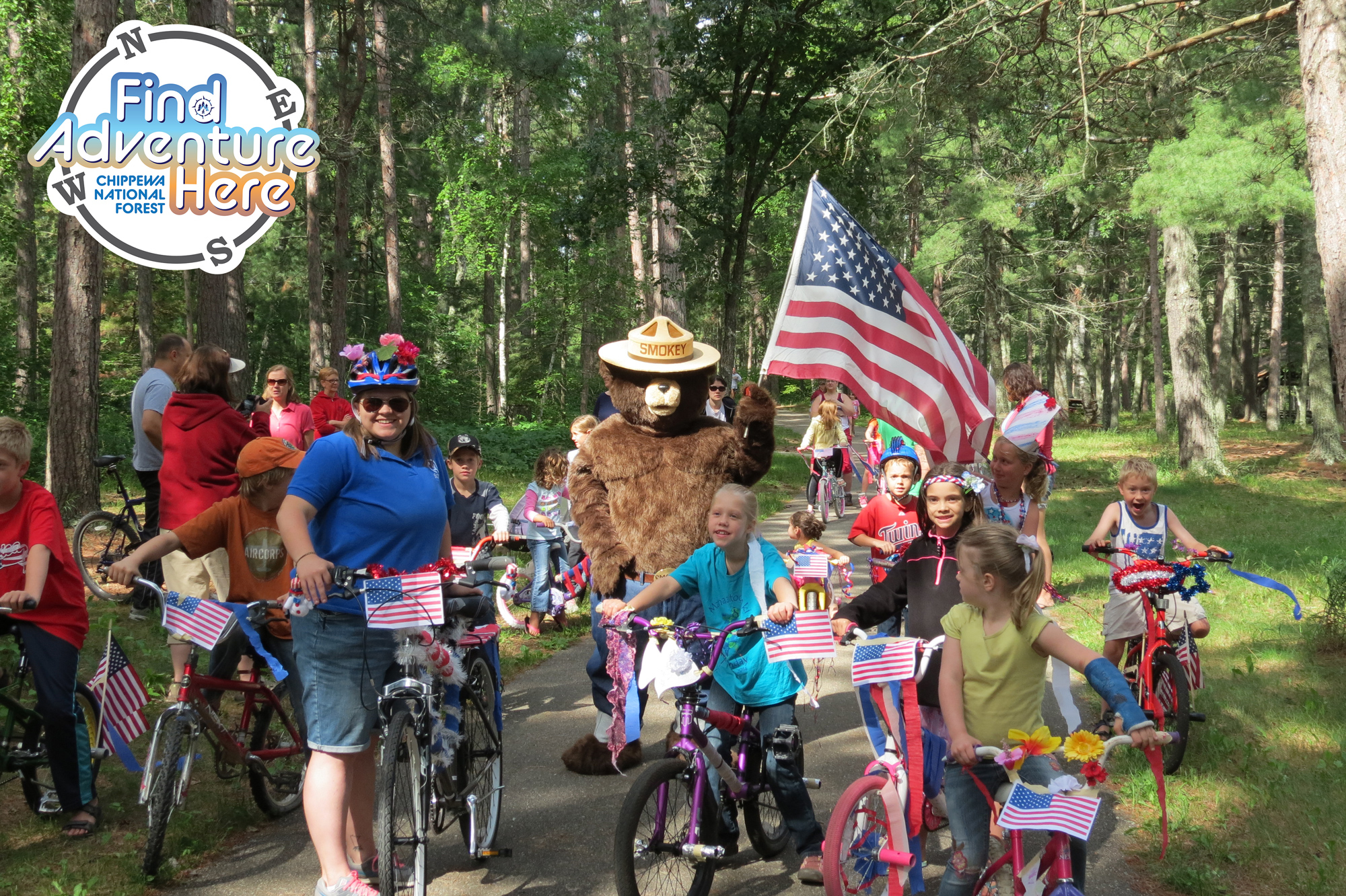 A bike parade with Smokey Bear with a Find Adventure Here Chippewa National Forest icon.