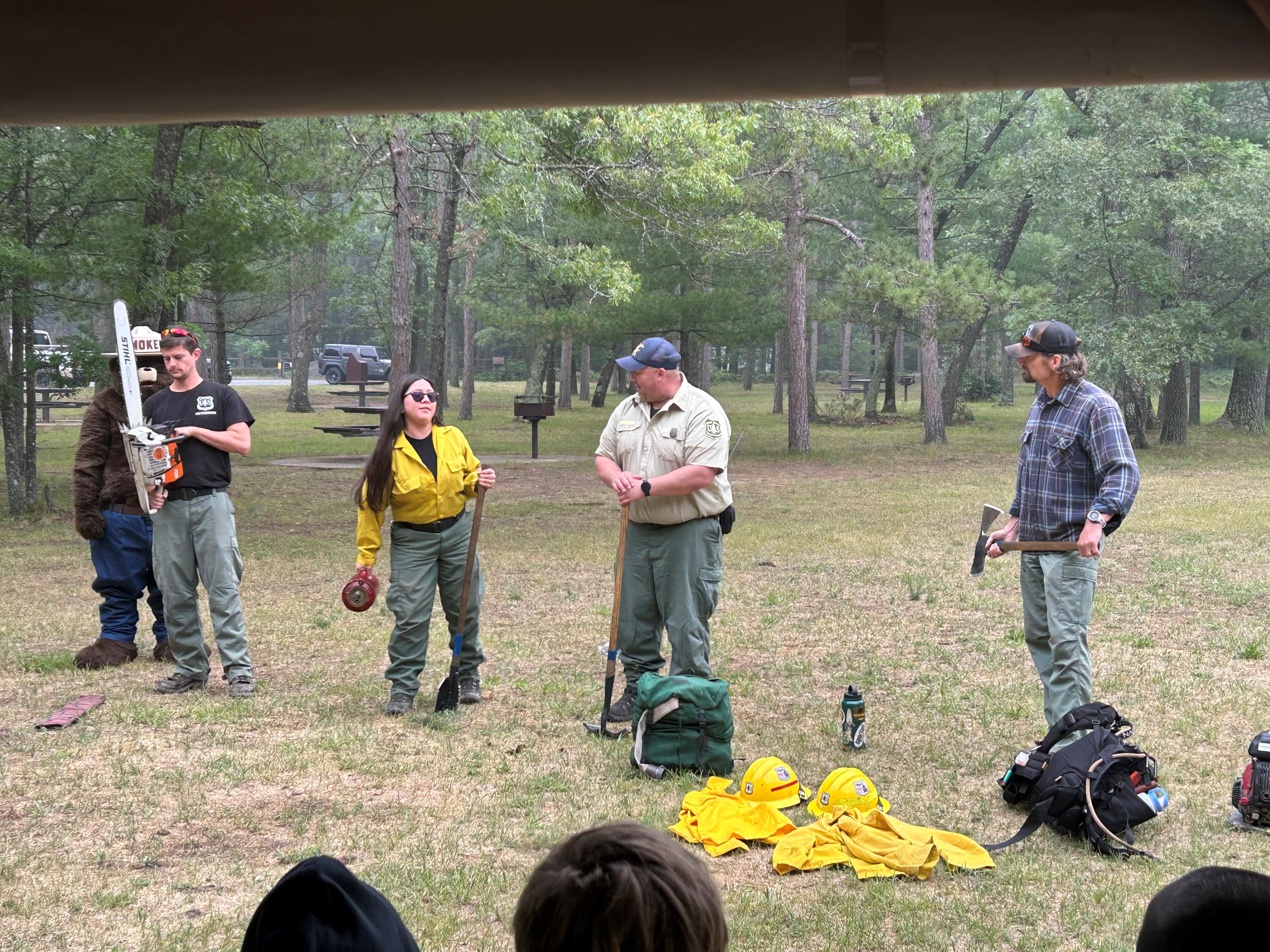 Four firefighters showing tools for firefighting with Smokey Bear.