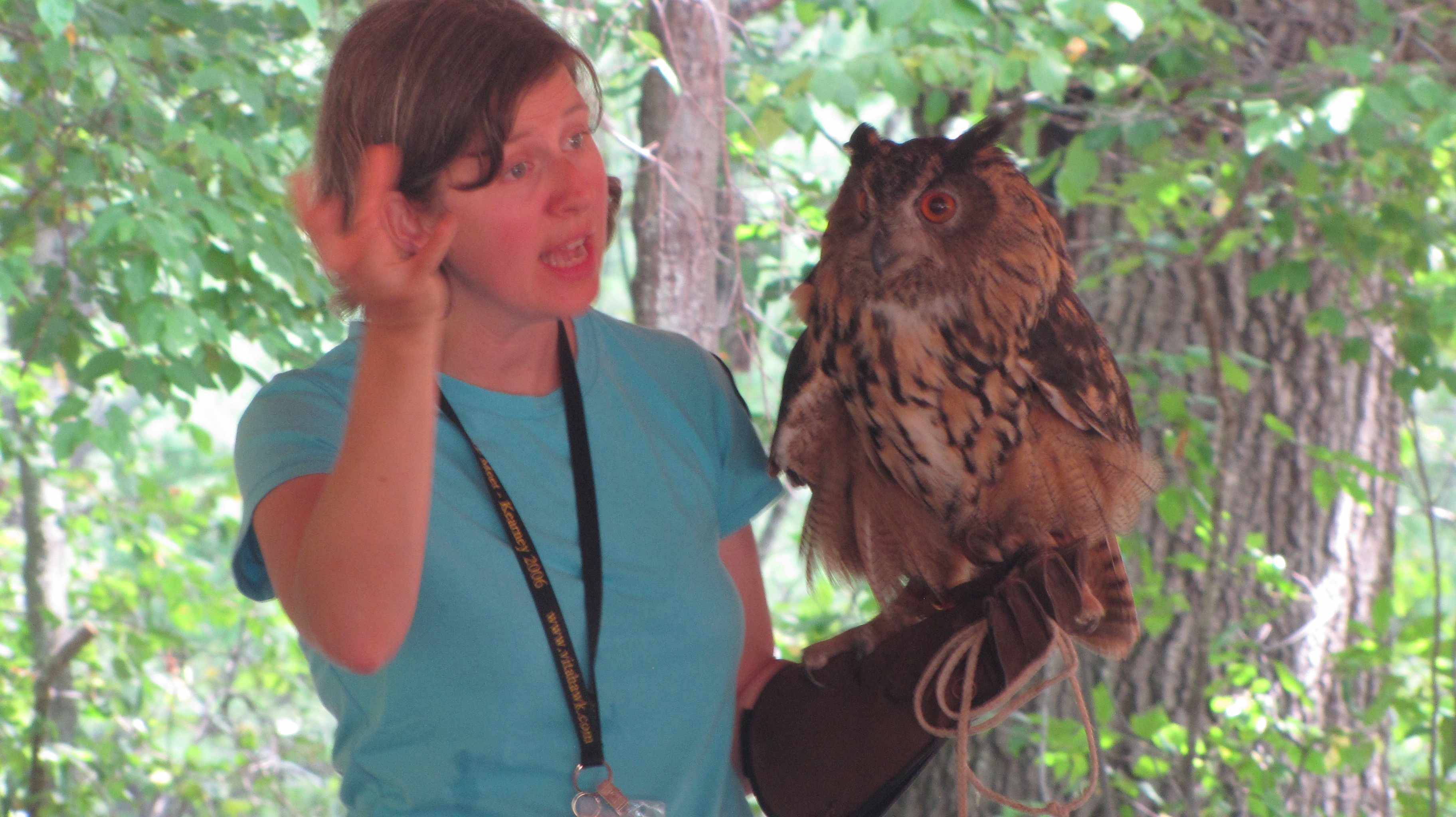 Woman holding an owl by its talons on her gloved hand.