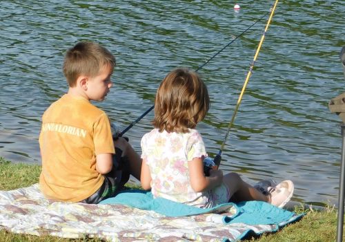 two kids sitting on a blanket fishing in a lake