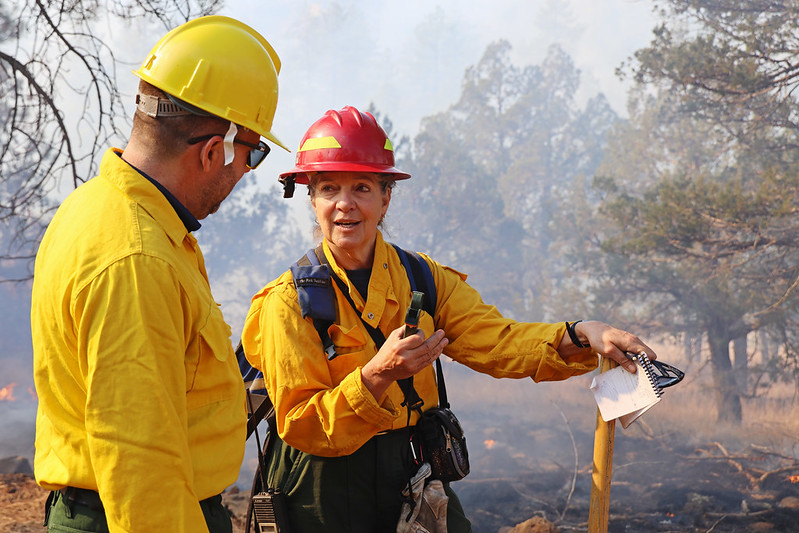 A female fire ecologist in fire gear speaks to another fire employee, a male meteorologist