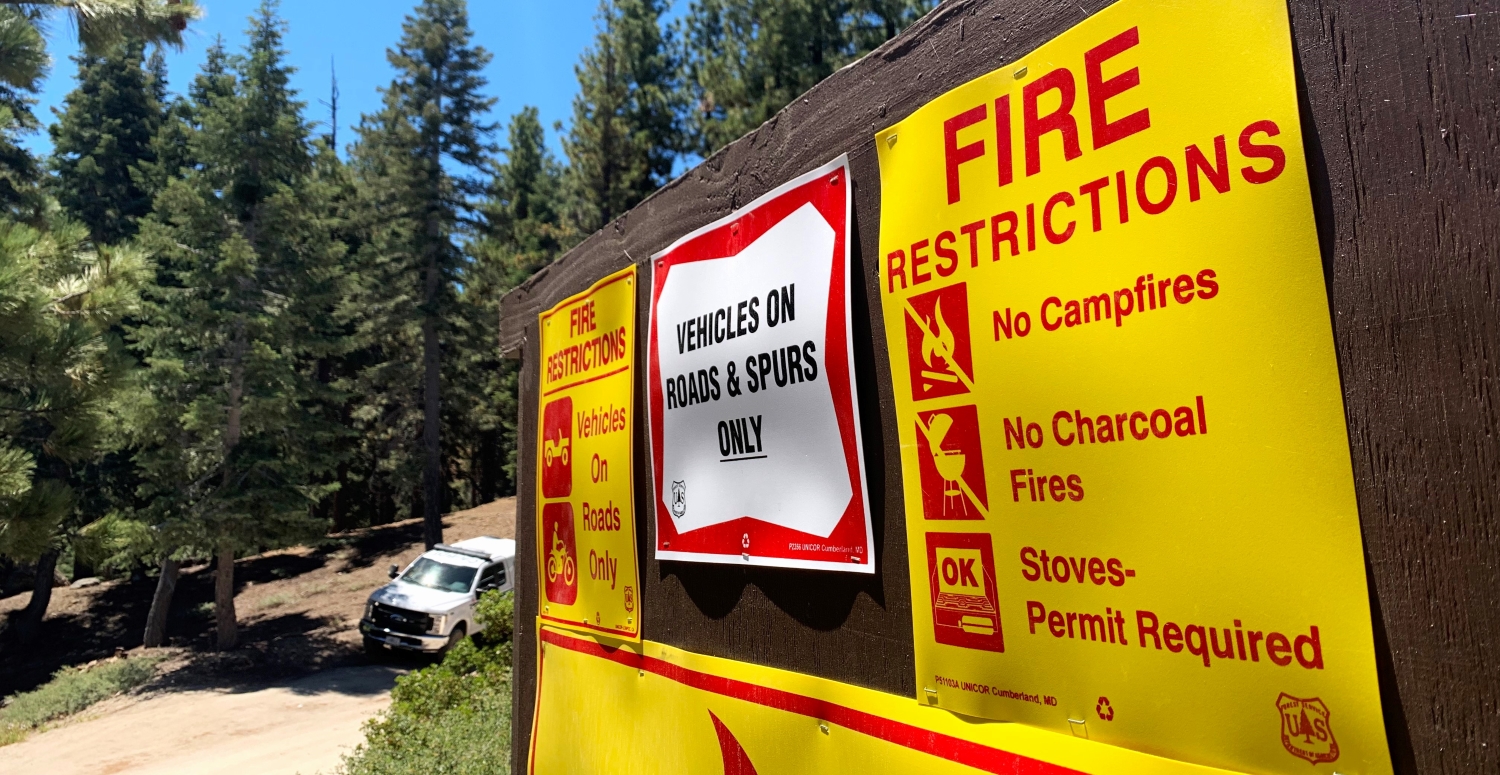 A brown sign has several posters that provide information about fire restrictions.