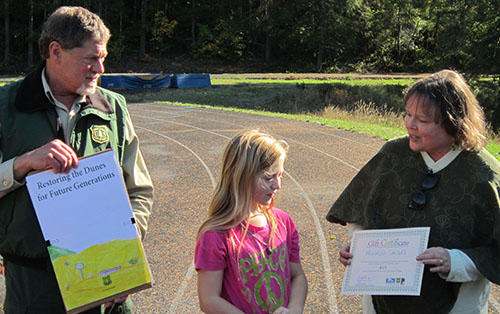 Fourth-grader Hannah Smoldt receives her award for her winning Oregon Dunes sign