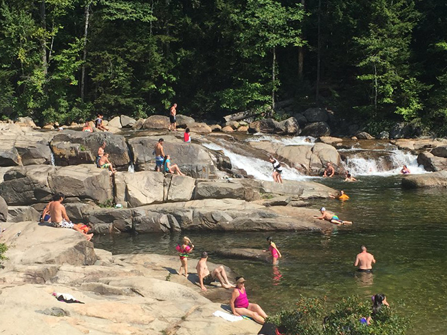 A low falls area on the forest full of people swimming and lounging on the rocks.