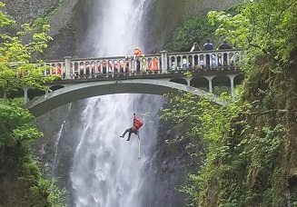 A person hangs off belay in front of Multnomah Falls.