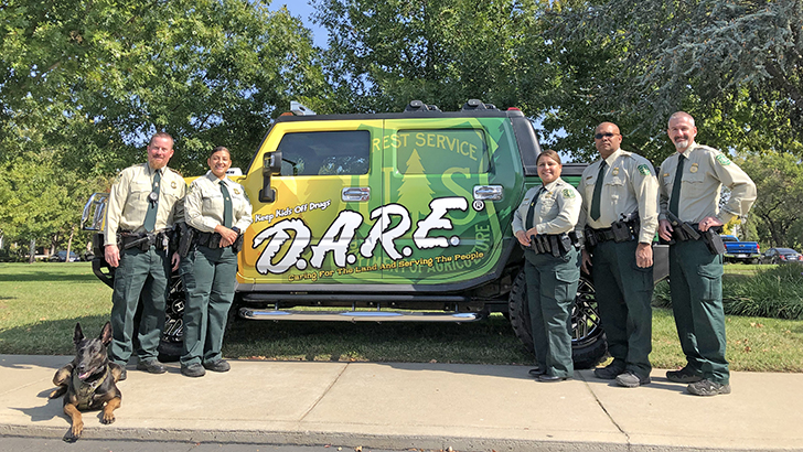 Forest Service law enforcement officers stand in front of decal-painted D.A.R.E. vehicle.