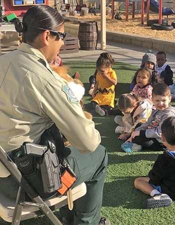 A female Forest Service law enforcement officer sits and reads to a kindergarten class about safety.
