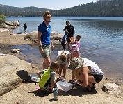 Kids and adults on shore of Lake Alpine looking at creatures in a bucket they caught in the lake.