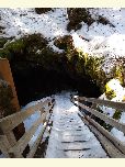 Snow covered staircase leads down into a darkened cave.