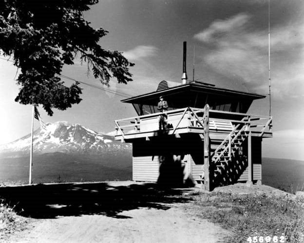 Black and white photo of an old fire lookout with a person standing on its deck