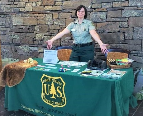 A Forest Service employee holds out arms at a tabling event