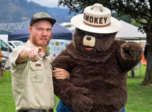 A forest ranger tand next to Smokey Bear and points at the viewer.